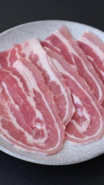 Baharat ve otlarla dilimlenmiş taze çiğ domuz pastırması ve koyu beton bir arka plan.