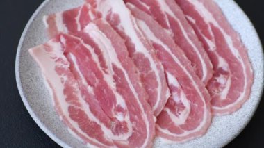 Baharat ve otlarla dilimlenmiş taze çiğ domuz pastırması ve koyu beton bir arka plan.