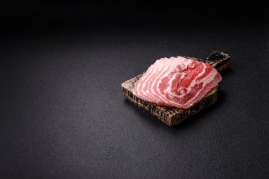 Baharat ve otlarla dilimlenmiş taze çiğ domuz pastırması ve koyu beton bir arka plan.