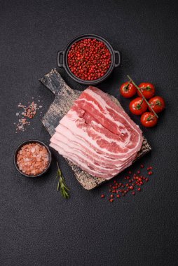 Baharat ve otlarla dilimlenmiş taze çiğ domuz pastırması ve koyu beton bir arka plan.