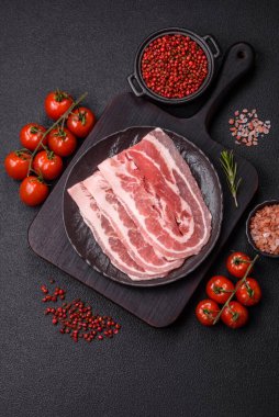Baharat ve otlarla dilimlenmiş taze çiğ domuz pastırması ve koyu beton bir arka plan.