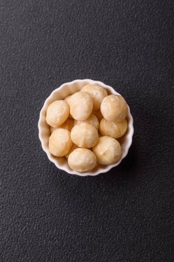 Koyu beton arka planda seramik kasede lezzetli, besleyici Macadamia fındıkları.