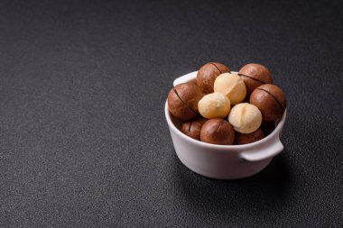 Koyu beton arka planda seramik kasede lezzetli, besleyici Macadamia fındıkları.