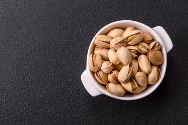 Koyu beton arka planda seramik kasede lezzetli, besleyici fıstıklar.