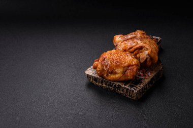 Tuz, baharat ve otlarla pişirilmiş lezzetli sulu tavuk butları koyu beton arka planda seramik bir tabakta.