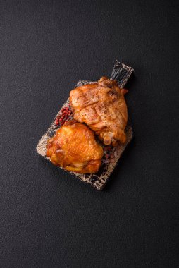 Tuz, baharat ve otlarla pişirilmiş lezzetli sulu tavuk butları koyu beton arka planda seramik bir tabakta.