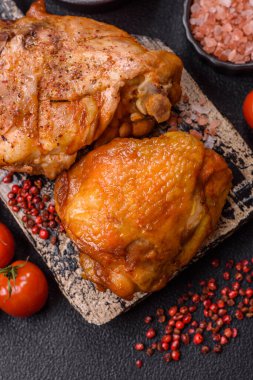 Tuz, baharat ve otlarla pişirilmiş lezzetli sulu tavuk butları koyu beton arka planda seramik bir tabakta.