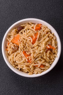 Lezzetli taze pilav, pirinç, havuç, et, soğan, baharat ve böğürtlen ile koyu beton arka planda seramik bir tabakta.