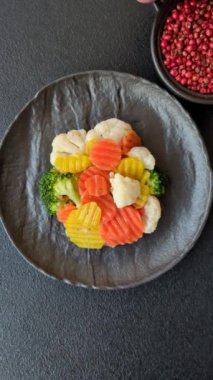 Delicious fresh vegetables steamed carrots, broccoli, cauliflower on a black plate on a dark concrete background