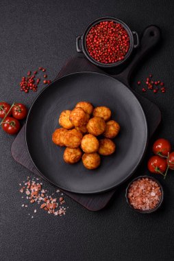 Delicious fried potato balls or croquettes with salt, spices and herbs on a dark concrete background