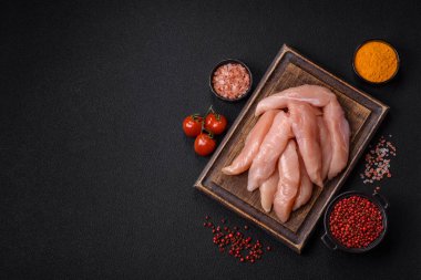 Çiğ tavuk filetosu, ahşap bir kesim tahtasının üzerinde baharat ve otlarla dilimlenmiş.