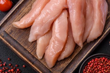 Çiğ tavuk filetosu, ahşap bir kesim tahtasının üzerinde baharat ve otlarla dilimlenmiş.