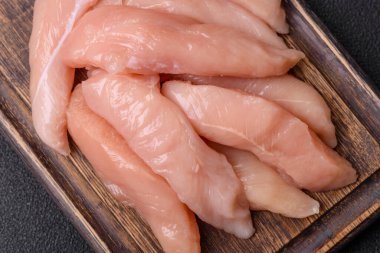 Çiğ tavuk filetosu, ahşap bir kesim tahtasının üzerinde baharat ve otlarla dilimlenmiş.