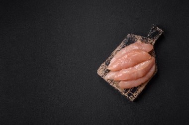 Çiğ tavuk filetosu, ahşap bir kesim tahtasının üzerinde baharat ve otlarla dilimlenmiş.