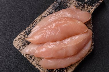 Çiğ tavuk filetosu, ahşap bir kesim tahtasının üzerinde baharat ve otlarla dilimlenmiş.