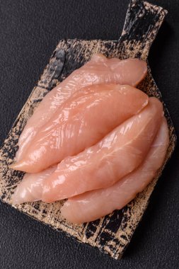 Çiğ tavuk filetosu, ahşap bir kesim tahtasının üzerinde baharat ve otlarla dilimlenmiş.