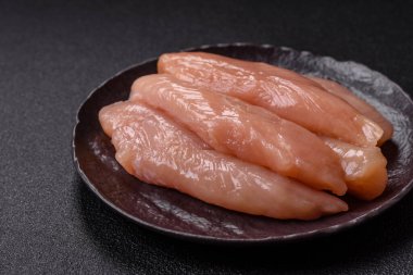 Çiğ tavuk filetosu, ahşap bir kesim tahtasının üzerinde baharat ve otlarla dilimlenmiş.