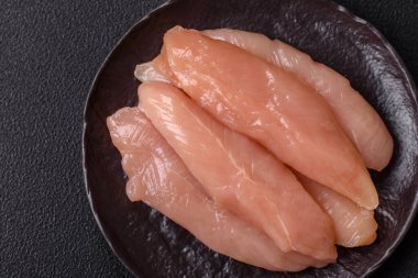 Çiğ tavuk filetosu, ahşap bir kesim tahtasının üzerinde baharat ve otlarla dilimlenmiş.