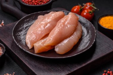 Çiğ tavuk filetosu, ahşap bir kesim tahtasının üzerinde baharat ve otlarla dilimlenmiş.