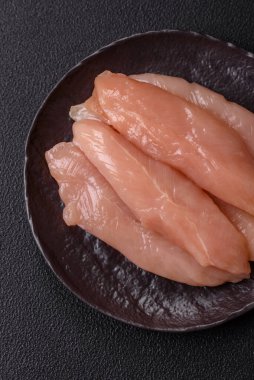 Çiğ tavuk filetosu, ahşap bir kesim tahtasının üzerinde baharat ve otlarla dilimlenmiş.