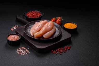 Çiğ tavuk filetosu, ahşap bir kesim tahtasının üzerinde baharat ve otlarla dilimlenmiş.