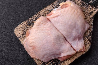 Taze çiğ tavuk butları, koyu beton arka planda tuz ve baharatlar.