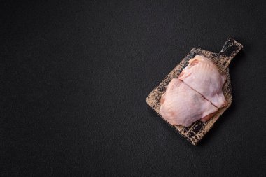 Taze çiğ tavuk butları, koyu beton arka planda tuz ve baharatlar.