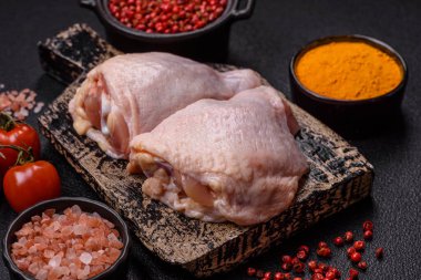 Taze çiğ tavuk butları, koyu beton arka planda tuz ve baharatlar.