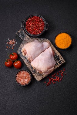 Taze çiğ tavuk butları, koyu beton arka planda tuz ve baharatlar.