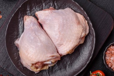 Taze çiğ tavuk butları, koyu beton arka planda tuz ve baharatlar.