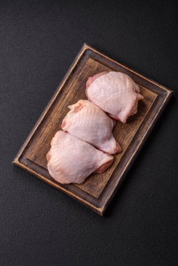 Taze çiğ tavuk butları, koyu beton arka planda tuz ve baharatlar.