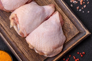 Taze çiğ tavuk butları, koyu beton arka planda tuz ve baharatlar.