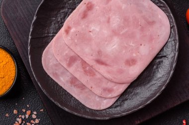Tuzlu ve baharatlı haşlanmış jambon. Koyu beton arka planda dilimler halinde kesilmiş.