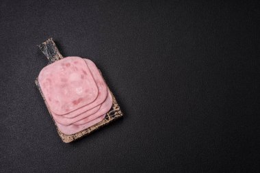 Tuzlu ve baharatlı haşlanmış jambon. Koyu beton arka planda dilimler halinde kesilmiş.