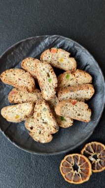 Taze pişmiş İtalyan cantuccini kurabiyeleri fındıklı ve şekerli meyveler koyu beton arka planda