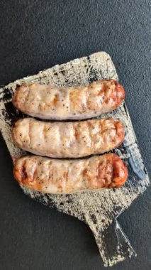 Koyu beton bir arka planda ızgarada tuzlu ve baharatlı sulu tavuk ya da domuz sosisi.