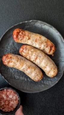 Koyu beton bir arka planda ızgarada tuzlu ve baharatlı sulu tavuk ya da domuz sosisi.