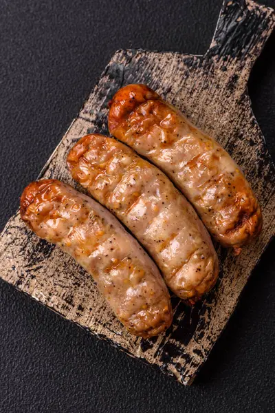 Koyu beton bir arka planda ızgarada tuzlu ve baharatlı sulu tavuk ya da domuz sosisi.