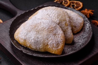 Meyve ve böğürtlenli tatlı hamur tatlısı koyu beton arka planda pudra şekeri serpiştirilmiş.