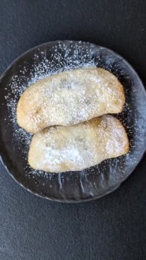 Meyve ve böğürtlenli tatlı hamur tatlısı koyu beton arka planda pudra şekeri serpiştirilmiş.