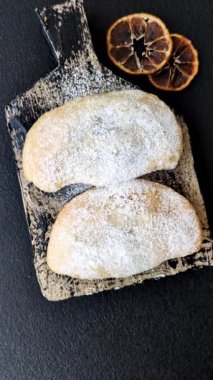 Meyve ve böğürtlenli tatlı hamur tatlısı koyu beton arka planda pudra şekeri serpiştirilmiş.