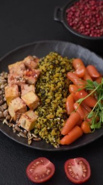 Soya peyniri, buğulanmış sebzeler, tahıllar, tohumlar ve baharatlar ile koyu beton bir arka planda.