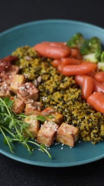 Soya peyniri, buğulanmış sebzeler, tahıllar, tohumlar ve baharatlar ile koyu beton bir arka planda.