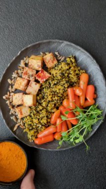 Soya peyniri, buğulanmış sebzeler, tahıllar, tohumlar ve baharatlar ile koyu beton bir arka planda.