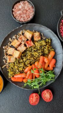 Soya peyniri, buğulanmış sebzeler, tahıllar, tohumlar ve baharatlar ile koyu beton bir arka planda.