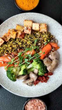 Soya peyniri, buğulanmış sebzeler, tahıllar, tohumlar ve baharatlar ile koyu beton bir arka planda.