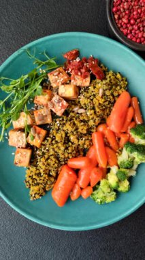 Soya peyniri, buğulanmış sebzeler, tahıllar, tohumlar ve baharatlar ile koyu beton bir arka planda.