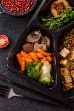 Soya peyniri, buğulanmış sebzeler, tahıllar, tohumlar ve baharatlar ile koyu beton bir arka planda.