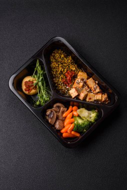 Soya peyniri, buğulanmış sebzeler, tahıllar, tohumlar ve baharatlar ile koyu beton bir arka planda.