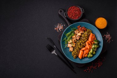 Soya peyniri, buğulanmış sebzeler, tahıllar, tohumlar ve baharatlar ile koyu beton bir arka planda.